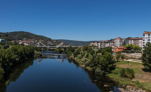 River amidst trees and cityscape against clear blue sky