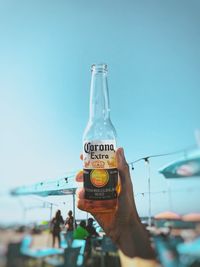 Person holding glass bottle against sky