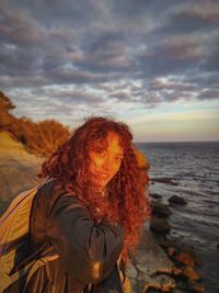 Woman standing by sea against sky during sunset