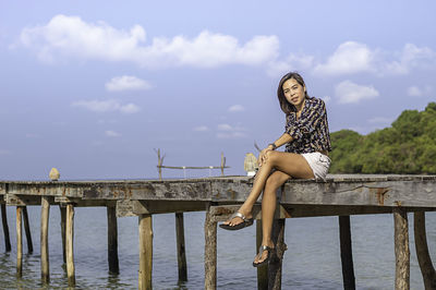 Woman sitting on pier over sea against sky