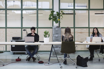 Two women and one man working at desk in creative office