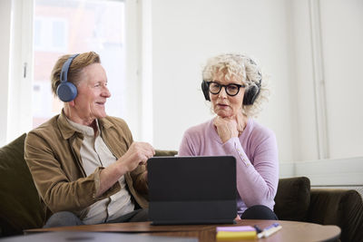 Senior man and woman talking to each other while sitting in living room and using digital tablet to edit podcast