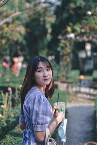 Portrait of young woman standing against trees