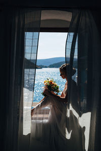 Woman with flower bouquet sitting on window at home