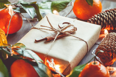 Close-up of gift by pine cone and oranges on illuminated table