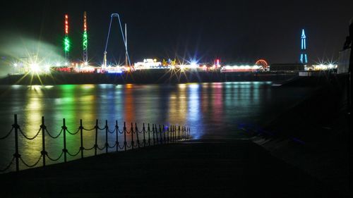 Illuminated city by river against sky at night