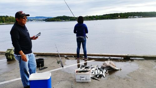 Man standing behind woman fishing in river