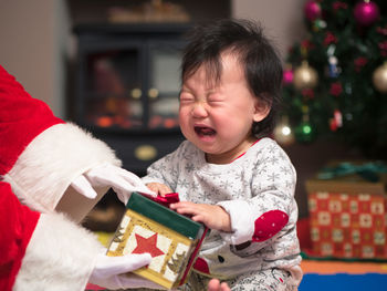 Cropped hands of santa claus giving gift to crying baby girl