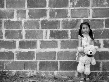 Portrait of a girl with toy standing against brick wall