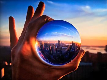 Close-up of hand against cityscape during sunset