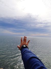 Cropped hand at sea against sky