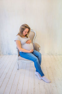 Pregnant woman sitting on chair against wall