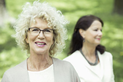 Portrait of smiling senior woman at park with friend in background