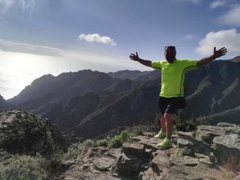Full length of man with arms outstretched standing on cliff against mountains