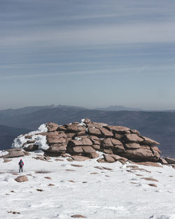 Distant view of hiker on snow covered mountain against sky