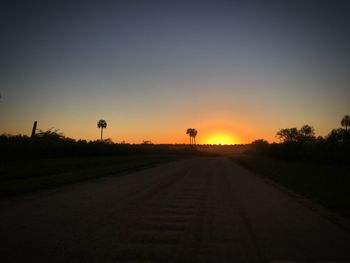 Road amidst silhouette landscape against sky at sunset
