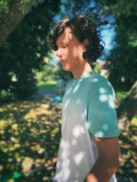 Side view of young woman standing against trees