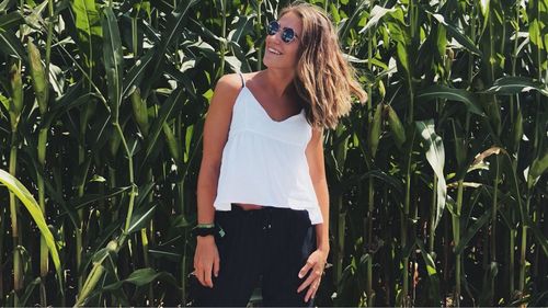 Smiling young woman in sunglasses standing against plants