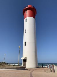 Lighthouse by building against clear blue sky
