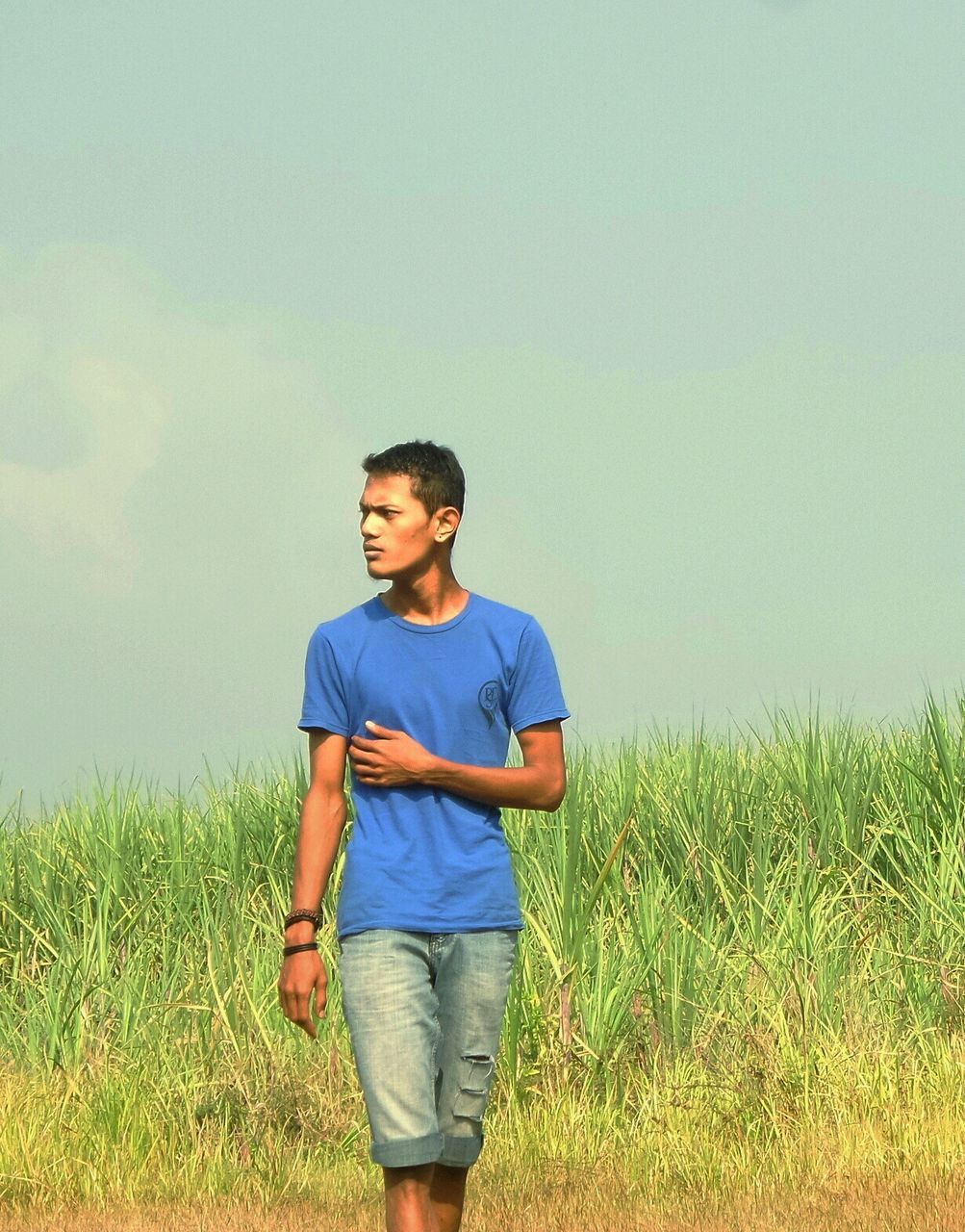 field, grass, lifestyles, casual clothing, standing, leisure activity, landscape, grassy, three quarter length, rural scene, agriculture, sky, farm, person, nature, full length, tranquility, tranquil scene