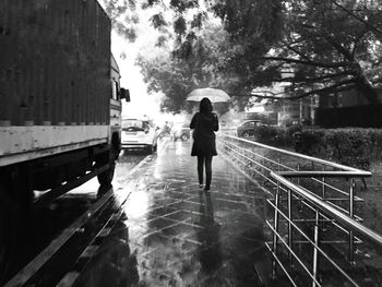 Rear view of a woman holding umbrella walking on wet street in rainy season