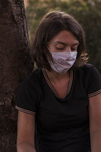 Portrait of young woman with mask standing on tree trunk