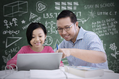 Girl with teacher at table against blackboard