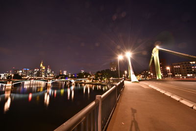 Illuminated city by river against sky at night