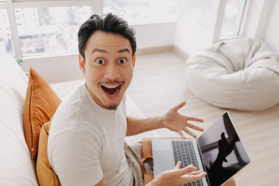 Portrait of smiling man gesturing while using laptop