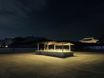 Illuminated building by sea against sky at dusk