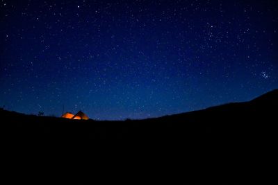 Illuminated tent on silhouette mountain against sky at night