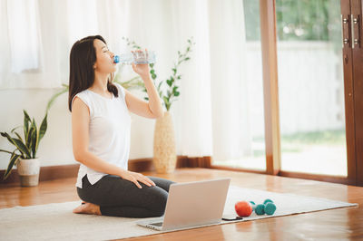 Woman drinking water while kneeling at home