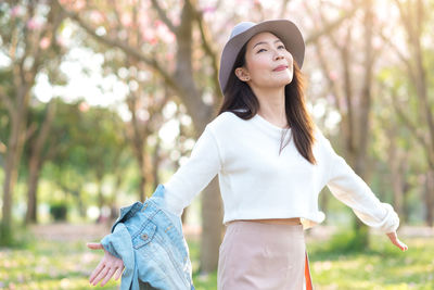 Smiling young woman arms outstretched standing in park