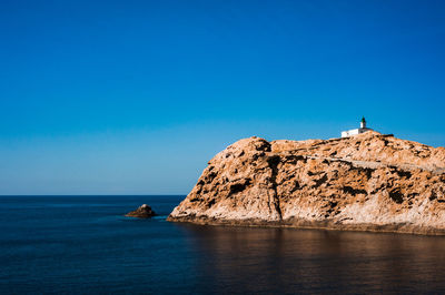 Rock formations by sea against clear blue sky