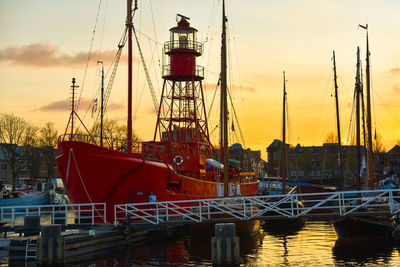 Sailboats moored at harbor against sky during sunset