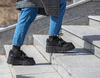 A girl in massive black boots, jeans and a checkered coat climbs up the granite stairs