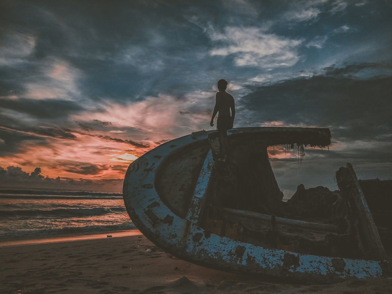 MAN STANDING ON ABANDONED BOAT AT SUNSET