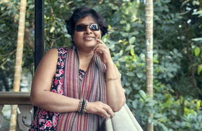 A young indian woman in sunglass and beautiful ethnic dress, enjoying view of garden from balcony