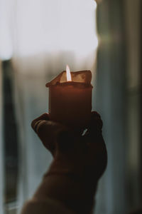 Cropped hand of woman holding candle against curtain