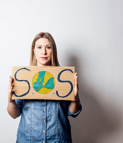 Portrait of smiling young woman reading book while standing against wall