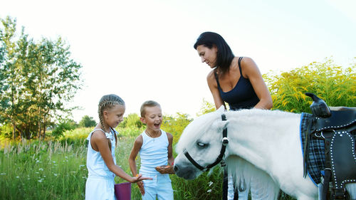 Children, a boy and a girl of seven years, fed a white pony, give to eat carrots. cheerful, happy