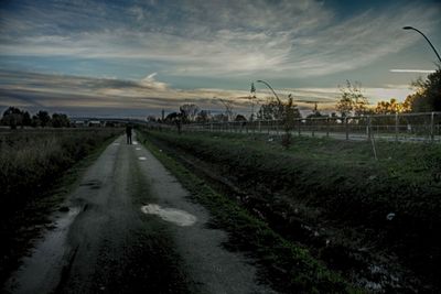 Dirt road amidst field against sky during sunset