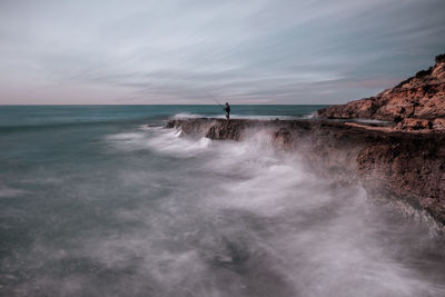 Mid distance view of man fishing in sea against sky