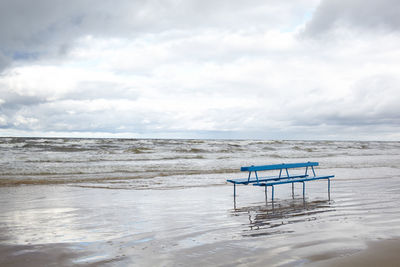 Empty bench at beach against sky