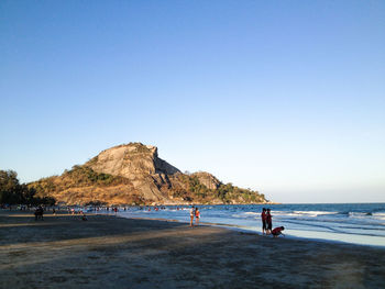 People at beach against clear blue sky