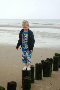 Boy walking on wooden post at beach against clear sky