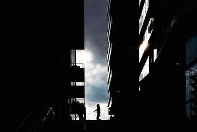 Silhouette man walking on illuminated building against sky at night