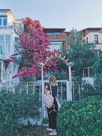 Woman standing by building against trees and plants