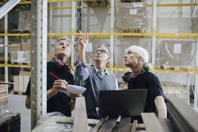 Senior entrepreneur discussing with colleagues while looking at planks in industry