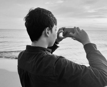 Portrait of man photographing sea against sky